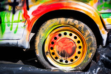 Shot Of Colorfully Painted Car Tire On An Old, Crashed Car Wreck. Kids Are Having Fun, Making Drawings And Graffiti Art, Paint On Wreck And Tires With Green, Red, Orange, Yellow, Blue Colors