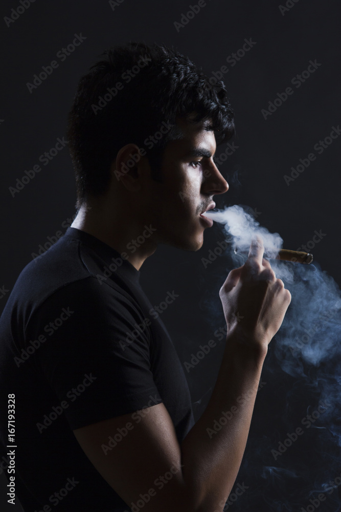 Side view of young man smoking against black background Stock Photo