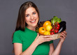 Smiling woman holding basket with vegetables.