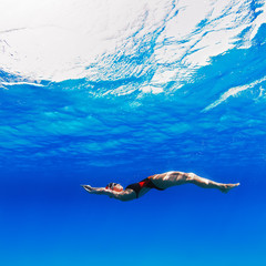 Wall Mural - professional female swimmer moving on her back underwater in blue