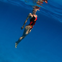 Wall Mural - professional sport swimmer floating up underwater in blue with small air bubbles on her face