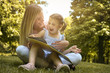 © liderina - Mother and daughter sitting on green grass and reading book together. Little girl sitting on mother lap.
