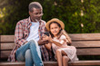 © LIGHTFIELD STUDIOS - smiling african american girl and her grandfather using smartphone sitting on bench together