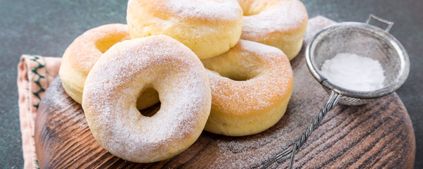 Wall Mural - Homemade baked donuts with powdered sugar on green background. Selective focus. Banner.