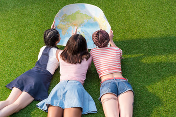 back view of young multiethnic women holding map while lying on green grass