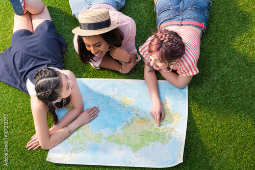 Zdjęcie XXL wysoki kąt widzenia wieloetnicznych dziewcząt patrząc na mapę, leżąc na zielonej trawie