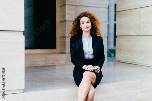 Attractive young woman wearing black formal suit, sitting crossed ...