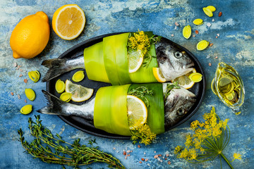 Wall Mural - Dorado wrapped in leek in baking form ready to cooking, preparation on rustic blue background with oil, herbs and spices. Top view, overhead