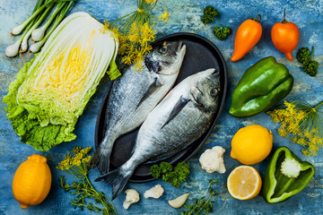 Wall Mural - Dorado in baking form ready to cooking, preparation on rustic blue background with fresh vegetables, herbs and spices. Top view, overhead