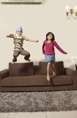 Wall Mural - Happy brother and sister jumping on sofa at home 