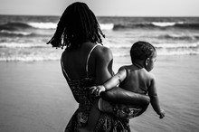 Mother Carrying Baby At Beach And Looking At Wave