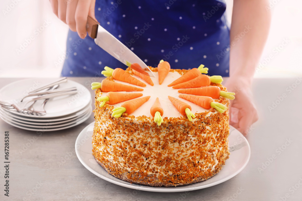 Young woman cutting delicious carrot cake on table