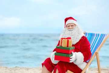 Authentic Santa Claus with gift boxes in deck chair on beach