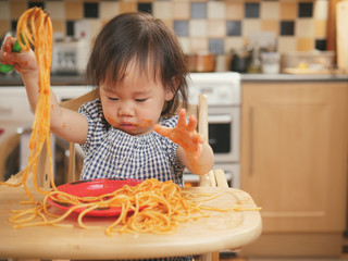 Wall Mural - baby girl eating messy spaghetti at home