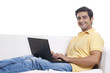 © IndiaPix - Portrait of handsome young man on sofa using laptop