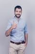 © deagreez - Success concept. Stylish young smiling bearded brunet is standing on pure gray background in smart casual outfit, shows like sign, his other handsis in pocket