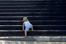 The One-year Child Climbs Up The Stairs. Cute Baby Boy In Hat Plays On The Stairs. The Concept Of Happy Childhood. Nature, Outdoors, Summer