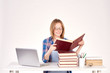 © pressmaster - Beautiful teenage schoolgirl sitting at desk with stack of books on it