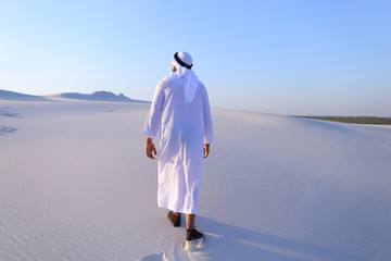 joyful muslim man walks on top of desert with smile on face on c