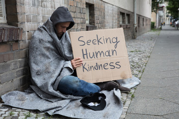 beggar showing seeking human kindness sign on cardboard