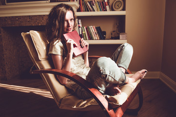 Wall Mural - Enjoying time at home. Pretty woman holding paper old book with anticipation in comfortable modern chair. Natural light. Cozy home. Bright sunny day. Knowledge and learning concept. Bookworm student