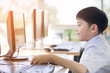 Happy asian boy in student uniform using computer at school .