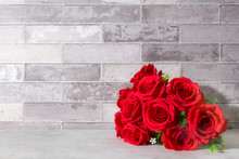 Artificial Red Rose Flower Bouquet On Table Gray Brick Wall Background.