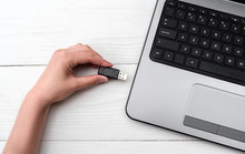 Hand Inserting USB Flash Drive Into Laptop Computer On White Background. Close Up Of Woman Hand Plugging Pendrive On Laptop At Home. Copying Data From Flash Drive To Laptop Computer
