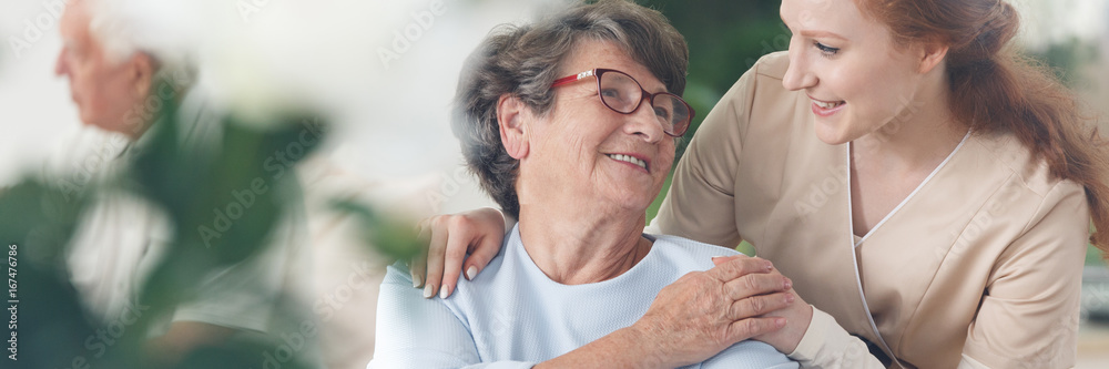 Caregiver comforting smiling senior woman - obrazy, fototapety, plakaty 