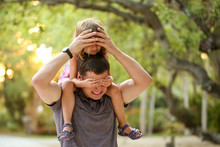 Father With Daughter On Shoulders Playfully Covering Each Others Eyes