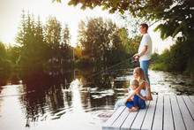 Young Happy Family With Kids Fishing In Pond In Summer