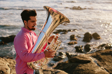 Outdoor Portrait of musician with tuba wind musical instrument. Sea shore, Atlantic Ocean