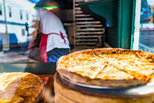 Closeup Of Fresh Handmade Pizza In Store Bakery On Display By Window With Chef Employee Working