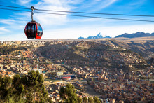 View Of La Paz Bolivia And The Peak Of Huayna Potosi Mountain In The Background With A Red Teleferico Cable Car Public Transportation System And Many Houses In The Distance With Beautiful Blue Skies