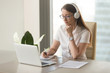 © fizkes - Focused attentive woman in headphones sits at desk with laptop, looks at screen, makes notes, learns foreign language in internet, online study course, self-education on web, consults client by video