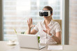 © fizkes - VR headset in use, businesswoman wearing virtual reality glasses for laptop and gesturing sitting at office desk, working with augmented reality apps, future computer technology for business concept