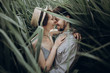 © sonyachny - happy hipster couple embracing at lake in cane. stylish rustic bride and groom, girl in fashionable modern dress and straw hat smiling at river in windy high reed. rustic wedding concept.