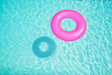 Bright Pink Float In Blue Swimming Pool, Ring Floating In A Refreshing Blue Swimming Pool With Waves Reflecting In The Summer Sun. Active Vacation Background. Lifesaver For Kid. Sunny Day At The Pool.
