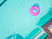 Top View Bright Pink Float In Blue Swimming Pool, Ring Floating In Refreshing Pool With Waves Reflecting In The Summer Sun. Active Vacation Background. Lifesaver For Kid. Sunny Day At The Pool Aerial