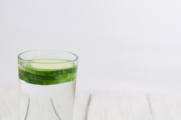 Three slices of green fresh cucumber in glass with water on old white wooden planks