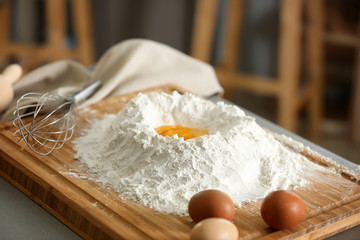 Wooden board with heap of flour and egg on kitchen table