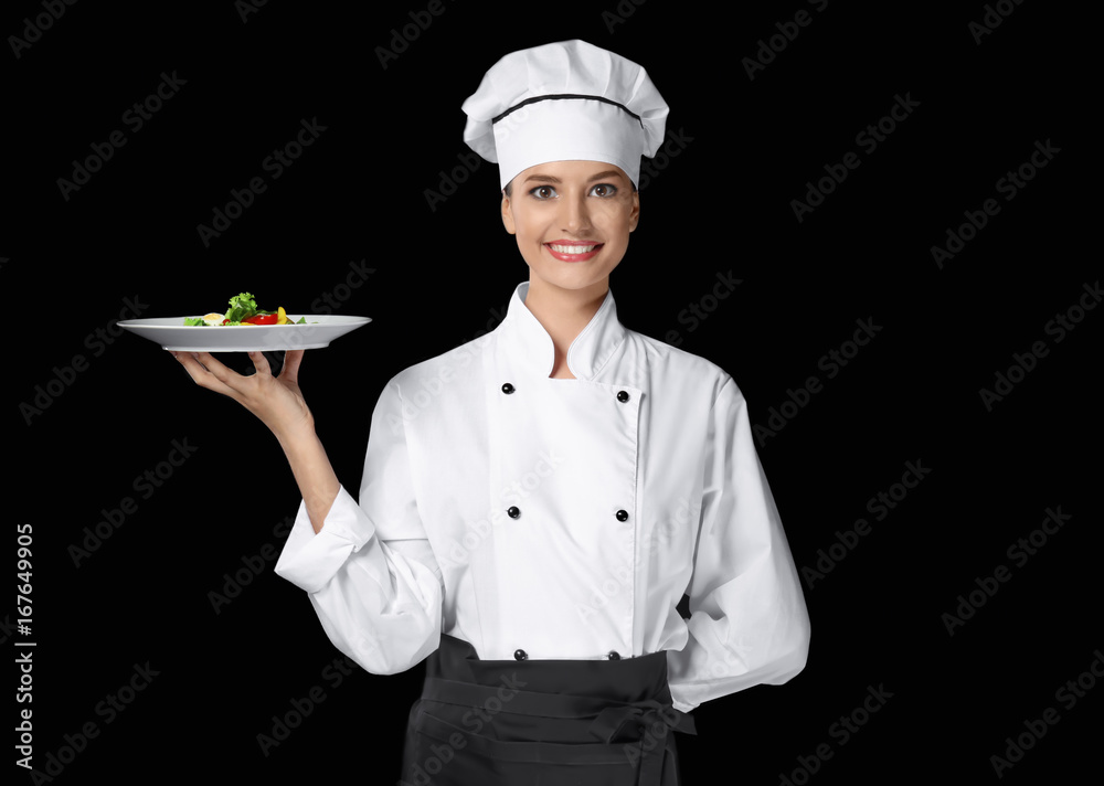 Young female chef holding plate with salad on dark background