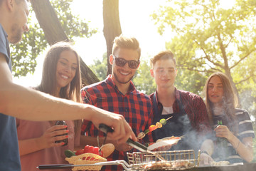 Happy friends grilling meat and enjoying barbecue party outdoors.