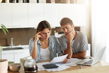 Serious man and female looking attentively in documents, trying to solve their financial problems. Young couple having family business, making financial annual report, calculating all figures