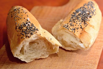 Two pieces of a white bread roll sprinkled with poppy seed and salt on a wooden cutting board.