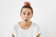 Joyful woman staring at camera with great surprisment not believing news which she just heard. Hipster girl with pink hair bun, wearing white loose T-shirt, looking with eyes full of disbelief