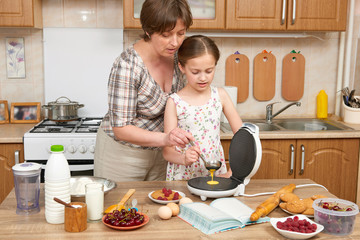 Woman and child girl baking waffles in home kitchen. Raw food and fruits. Healthy food concept.