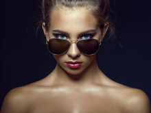Close Up Portrait Of Young Gorgeous Tanned Blue-eyed Model With Beautiful Make Up And Baby Hair Around Her Face Looking Straight Over Her Trendy Aviator Sunglasses. Isolated On Black Background