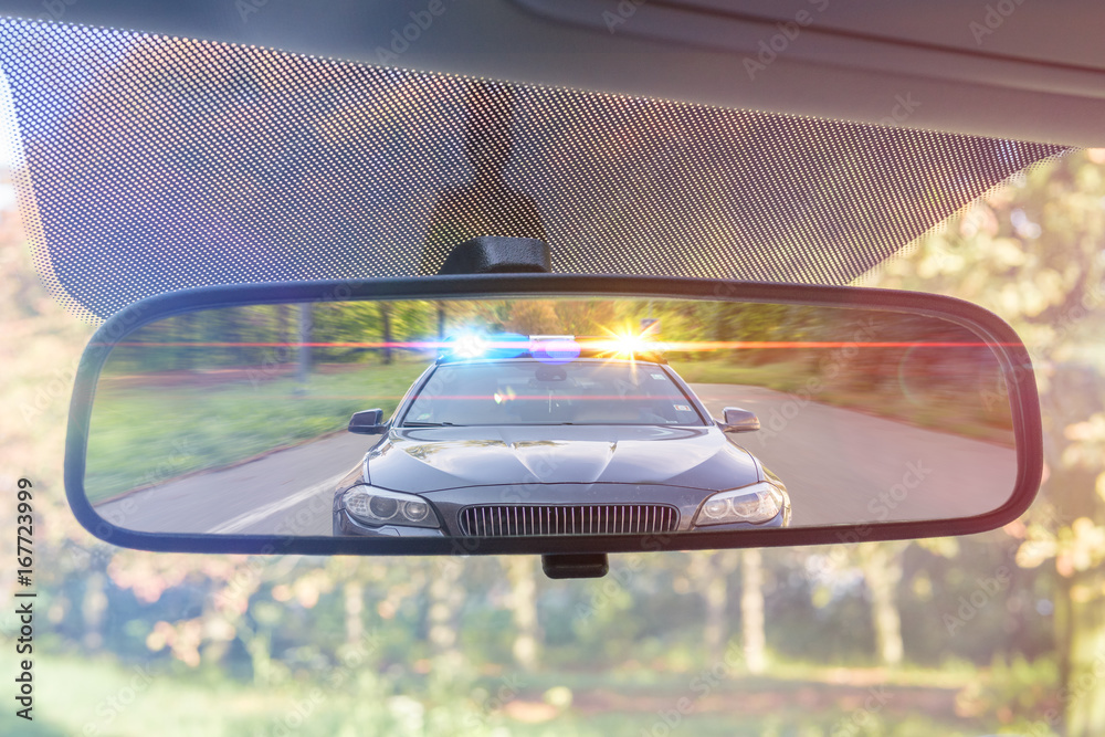 Cop Car In Rear Window View on rear mirror of a car. Police car with lights and siren is ...