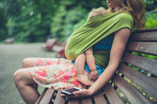Mother With Baby In Park Using Smartphone